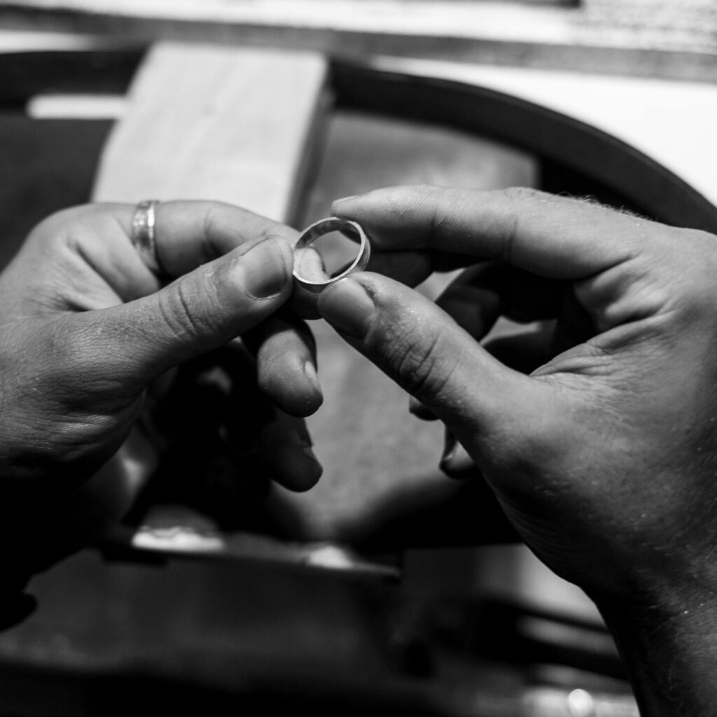 Monochrome photo showcasing hands crafting a ring, emphasizing craftsmanship.