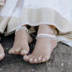 Close-up of two people in traditional attire, showcasing bare feet and anklets, sitting on a stone surface.